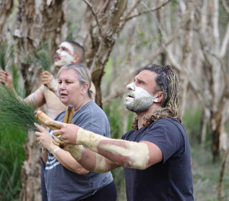Indigenous guides with traditional white face markings participating in a cultural ceremony in Coffs Harbour.