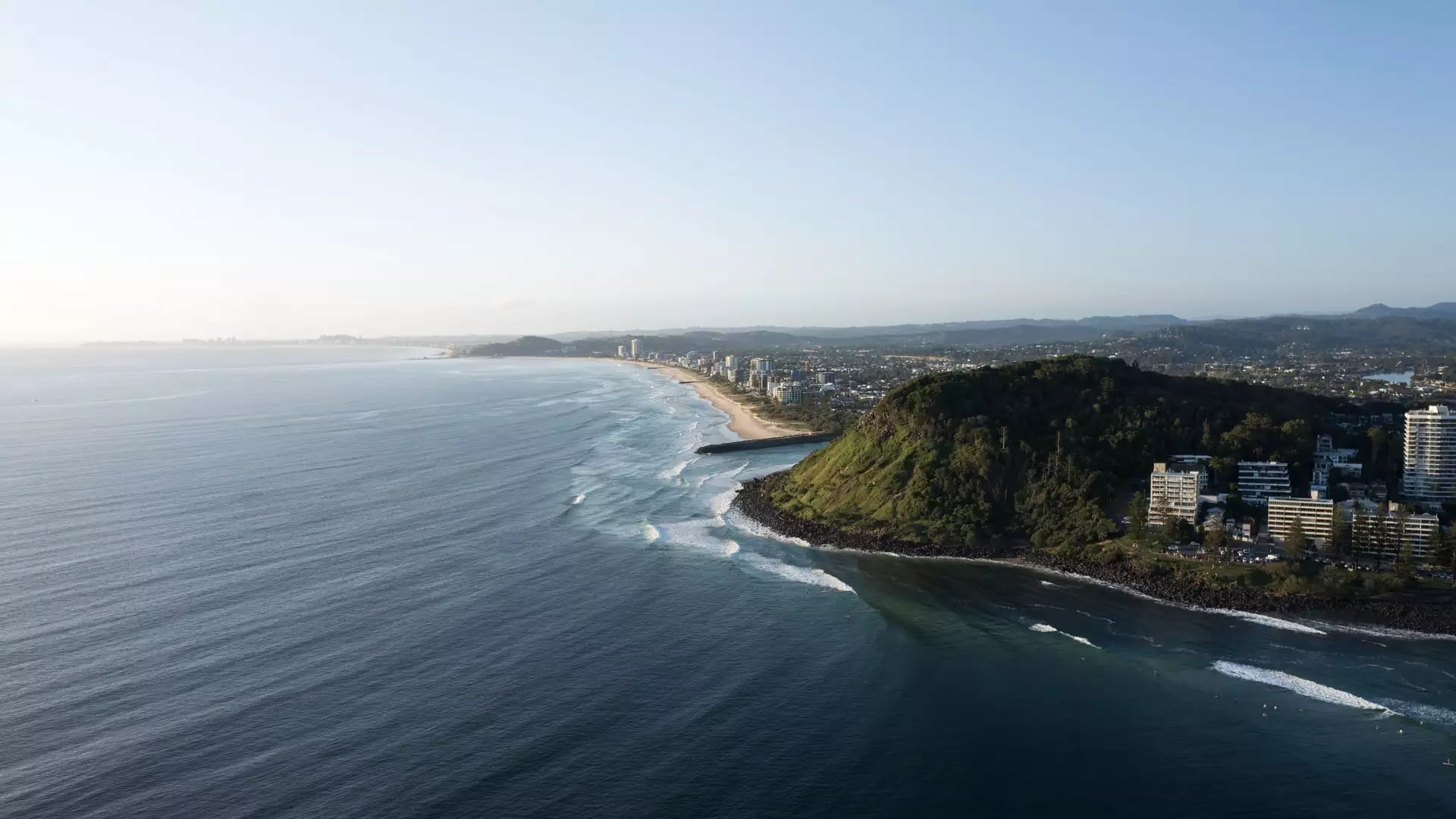 A wide aerial panorama looking north from Burleigh Head National Park, showing the coastline stretching toward the Surfers Paradise skyline.