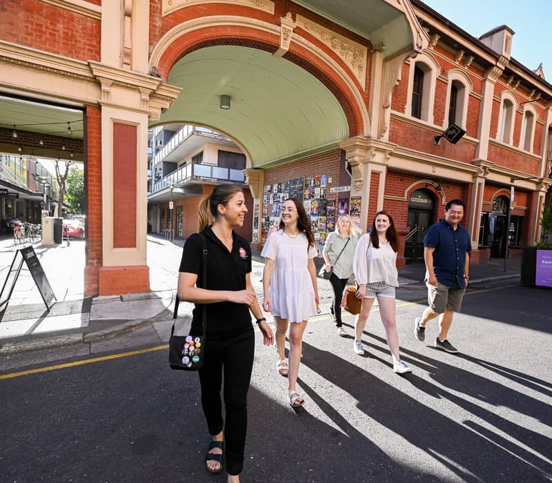 A tour guide and a group of travelers walking through a heritage brick archway in Adelaide.