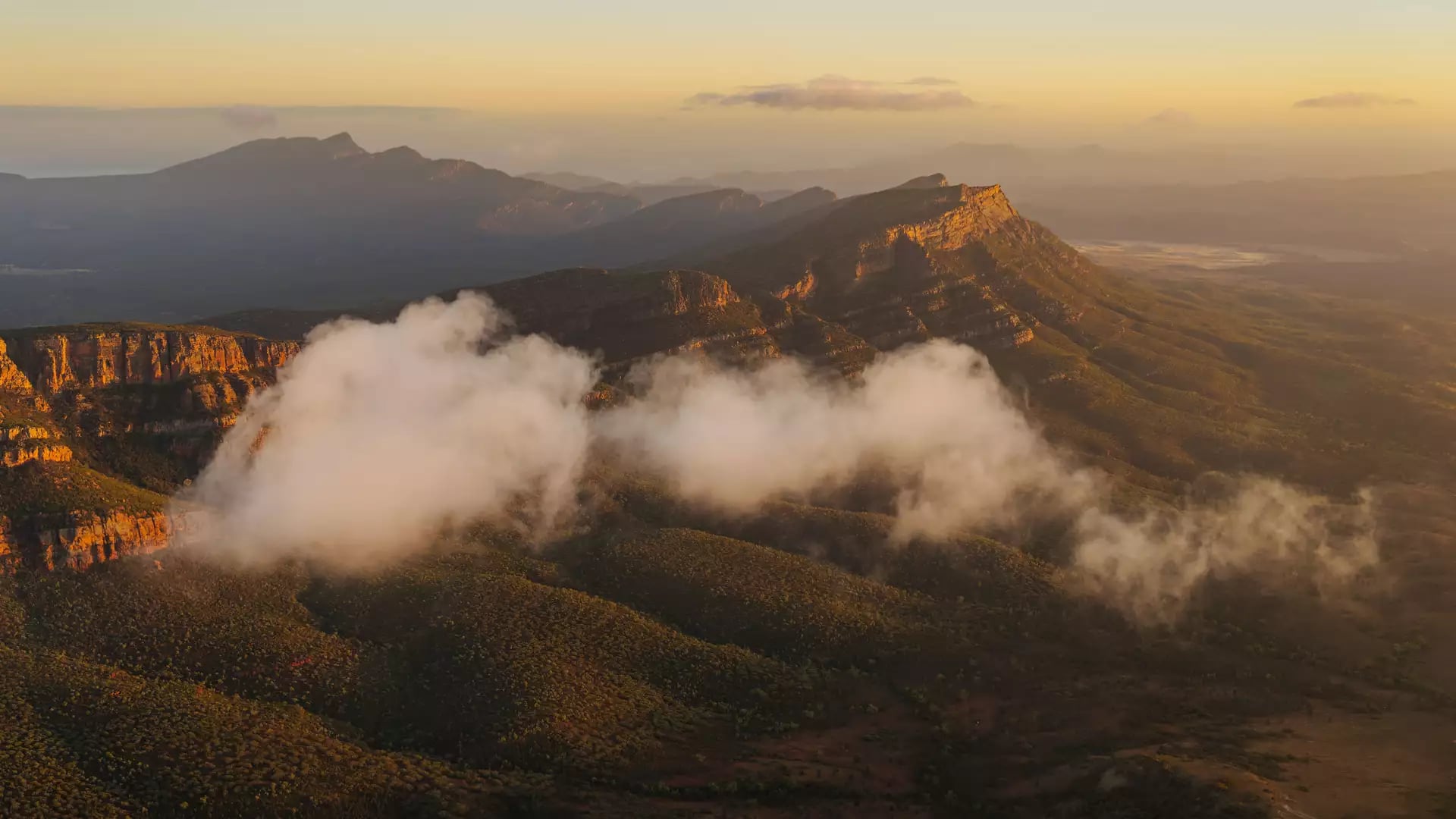 Low clouds drifting through the valleys of the Flinders Ranges mountains during golden hour.
