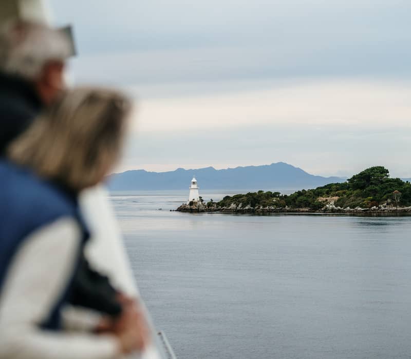 Tourists looking out from a boat at the white lighthouse on Bonnet Island in Tasmania.