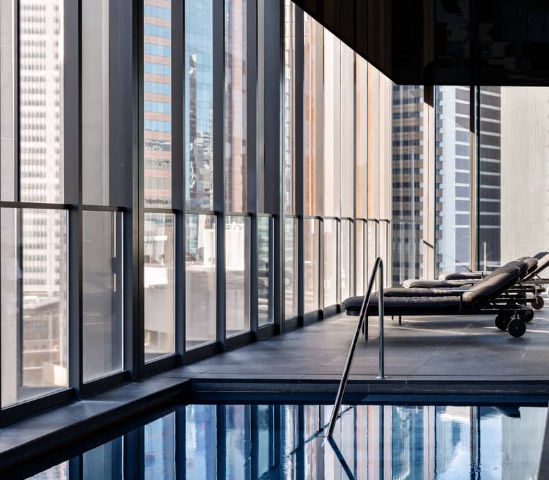 Contemporary hotel lounge with a grey sofa and yellow dining chairs overlooking the Sydney Tower and CBD skyline.