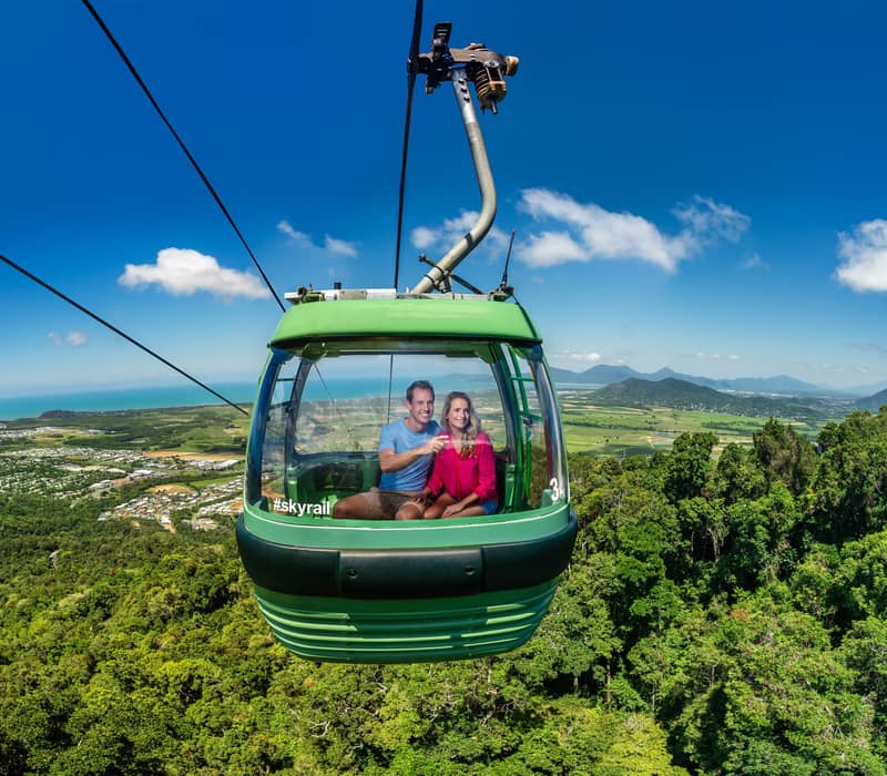Travelers in a green Skyrail gondola looking out over the Cairns rainforest canopy and ocean.