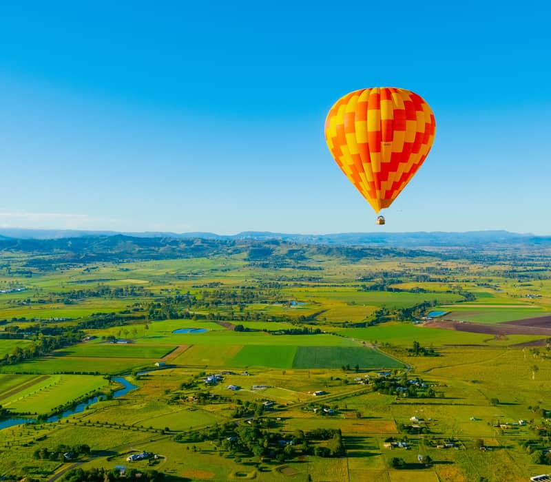 A vibrant hot air balloon flies over rural green farmland in the Canungra Valley region.