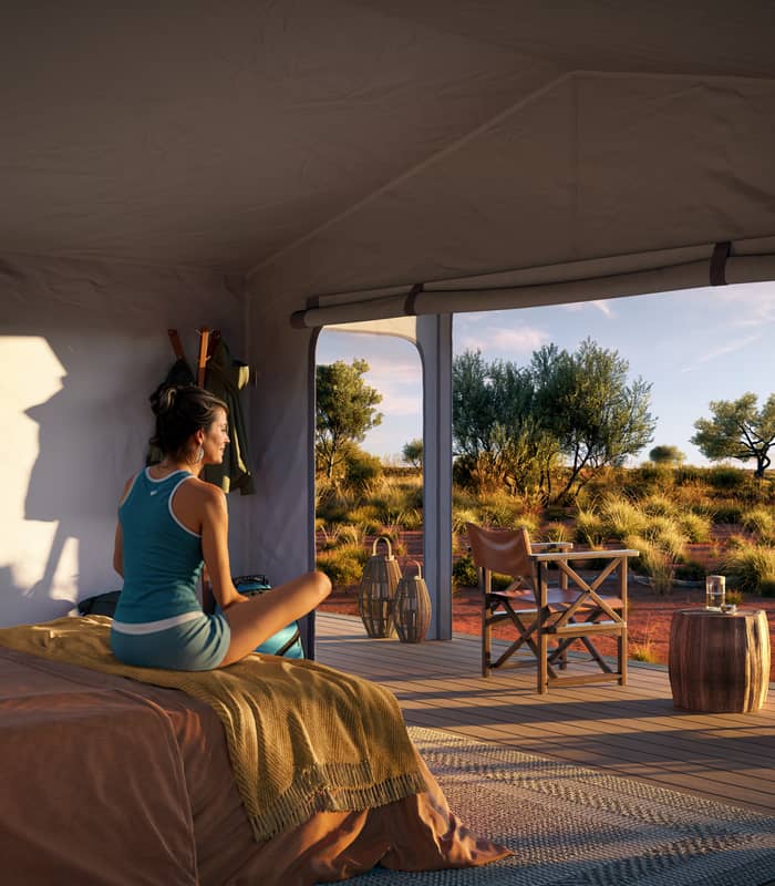 Luxury tent interior with a bed and open deck looking out over the Australian desert at sunset.