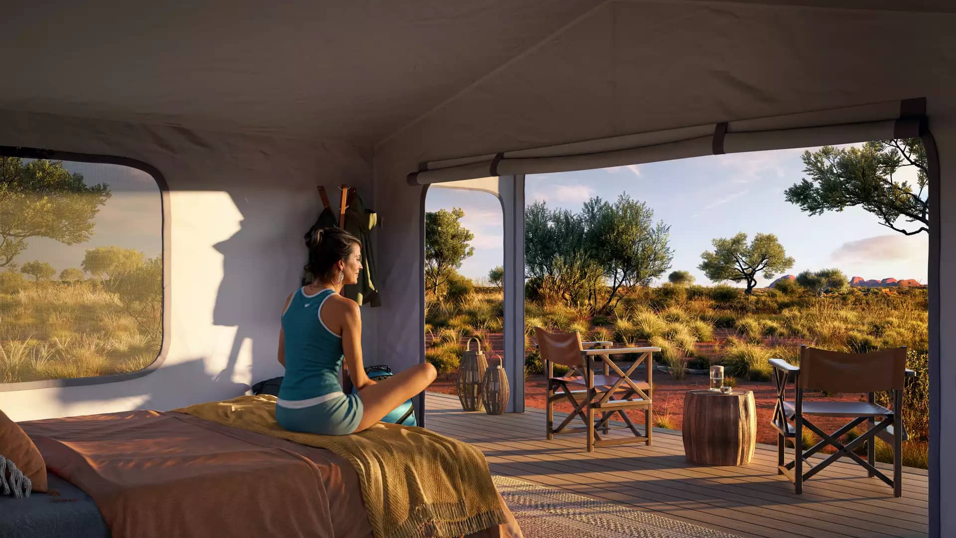 Luxury tent interior with a bed and open deck looking out over the Australian desert at sunset.
