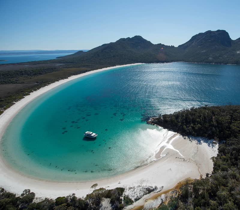High-angle panoramic view of Wineglass Bay showing the white sand beach and surrounding mountains.