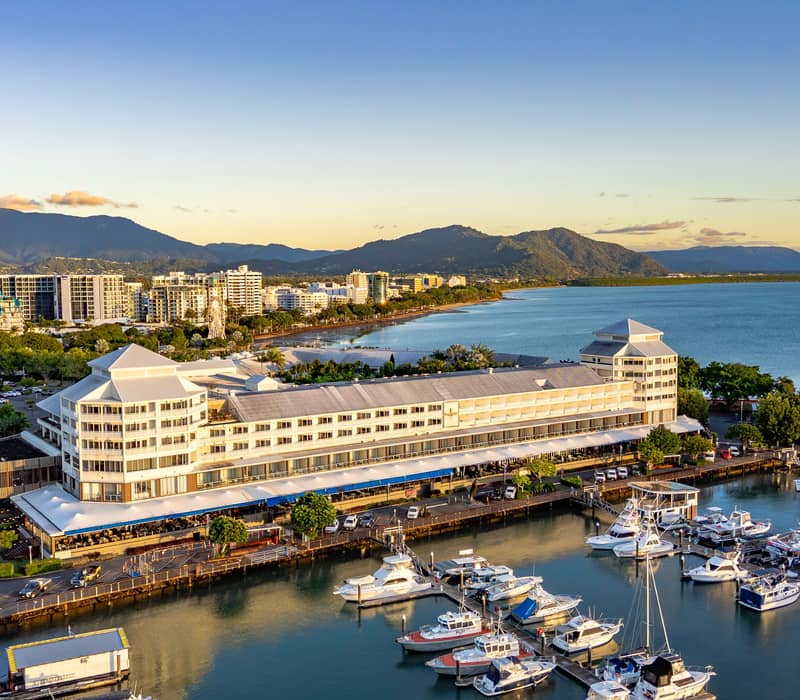 An aerial view of Cairns Marlin Marina at sunset with boats docked and mountains in the background.
