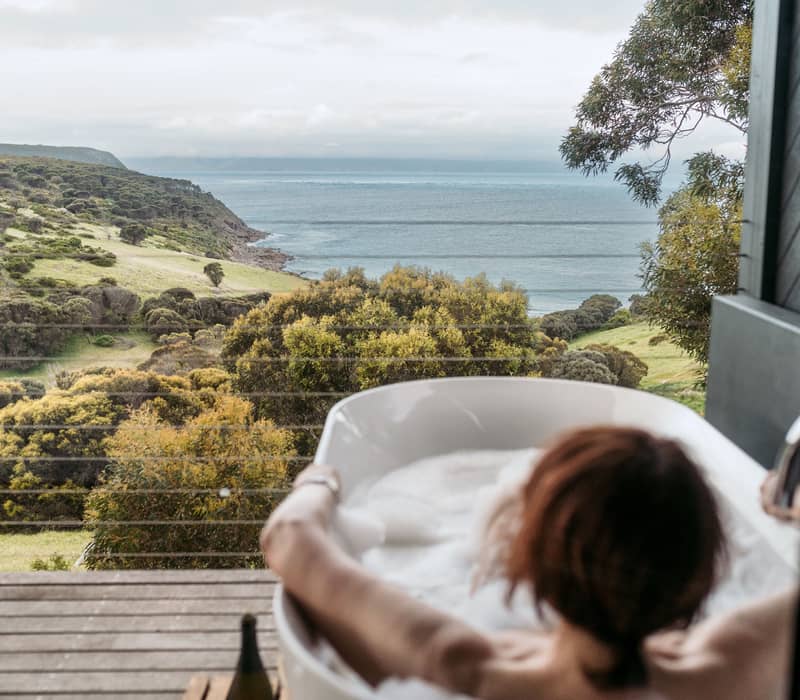 Person relaxing in a bathtub with a view of the Kangaroo Island coast from Sea Dragon.