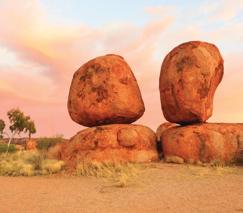 Two large, orange-hued rounded boulders balanced on top of each other at sunset in the Northern Territory outback.