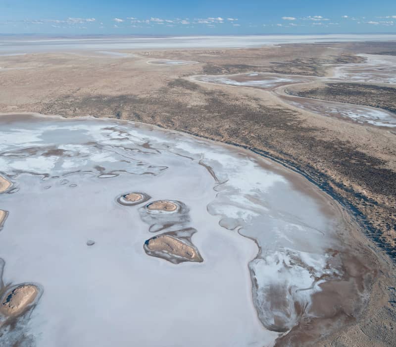 Aerial view showing the intricate white and brown textures of the Lake Eyre salt basin under a clear blue sky.