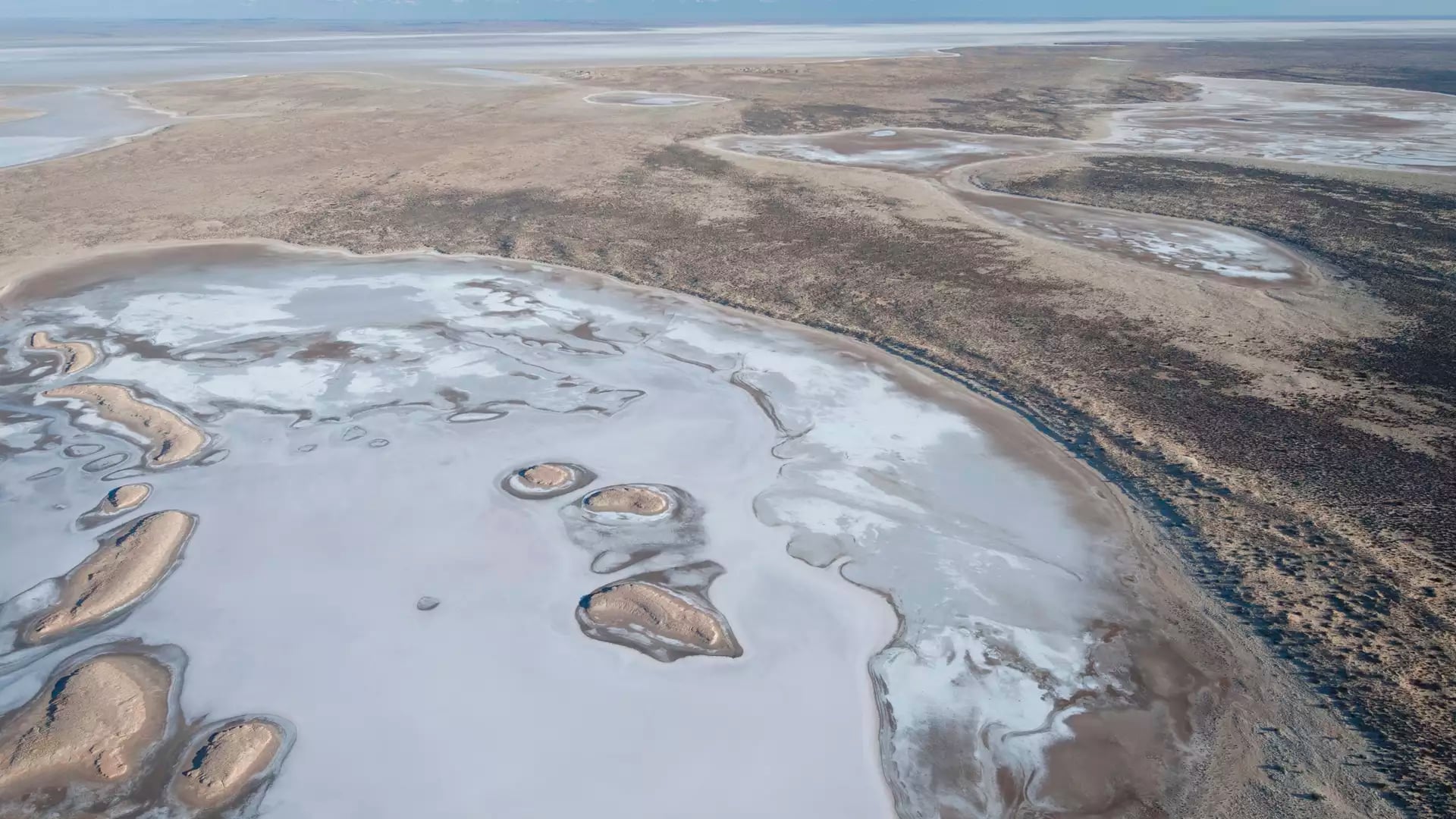 Aerial view showing the intricate white and brown textures of the Lake Eyre salt basin under a clear blue sky.