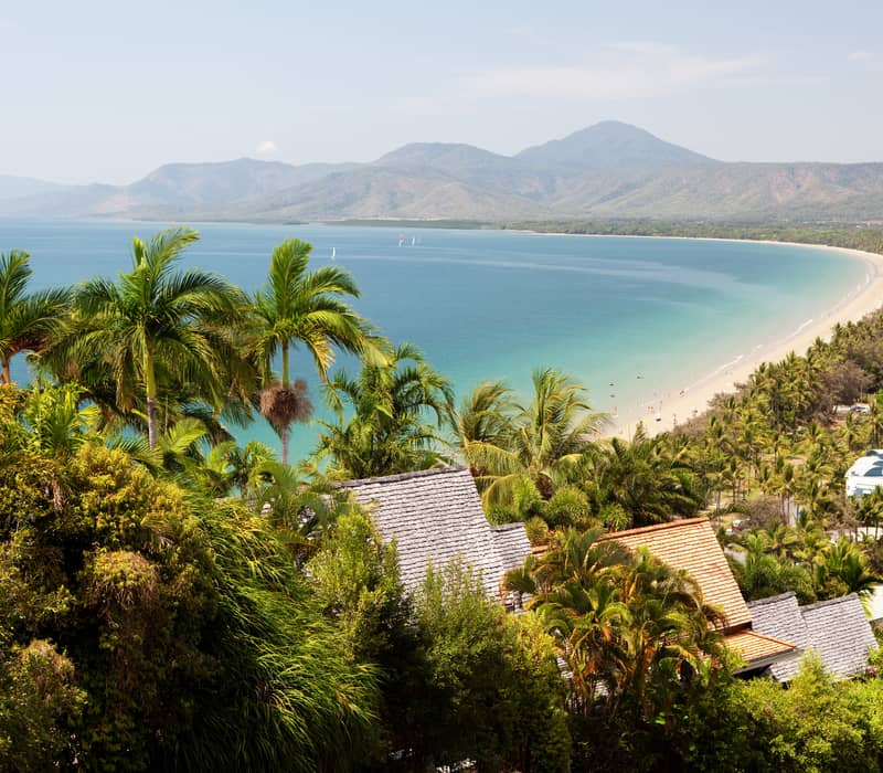 Elevated coastal view of a long sandy beach and green mountains meeting the blue ocean in Port Douglas, Queensland.