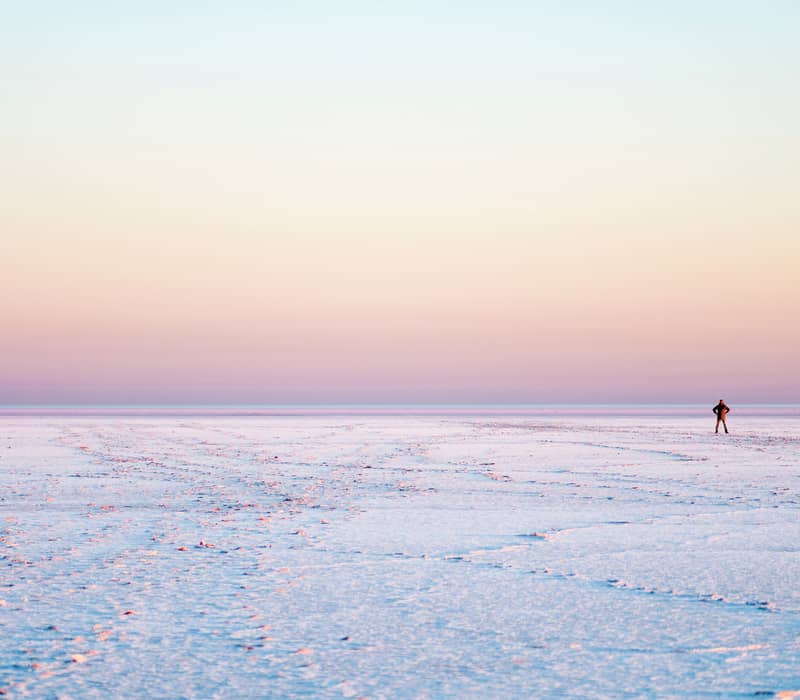 Wide-angle view of a person standing on a white salt crust plain under a pink and purple dusk sky in South Australia.