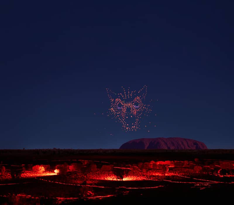 Glowing red and yellow circular light patterns on poles in the desert night with blue illuminated ripples on the ground.