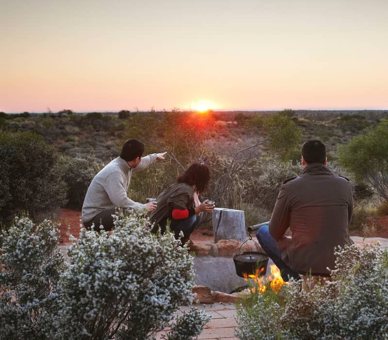 A group of people watching the sun rise over the Australian outback desert landscape near Uluru.