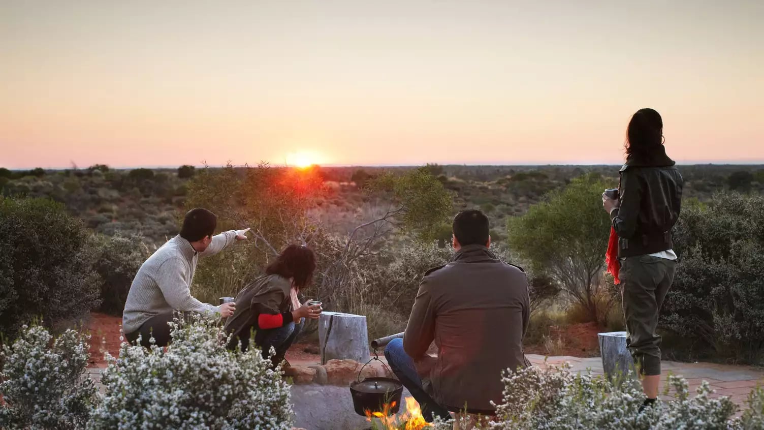A group of people watching the sun rise over the Australian outback desert landscape near Uluru.