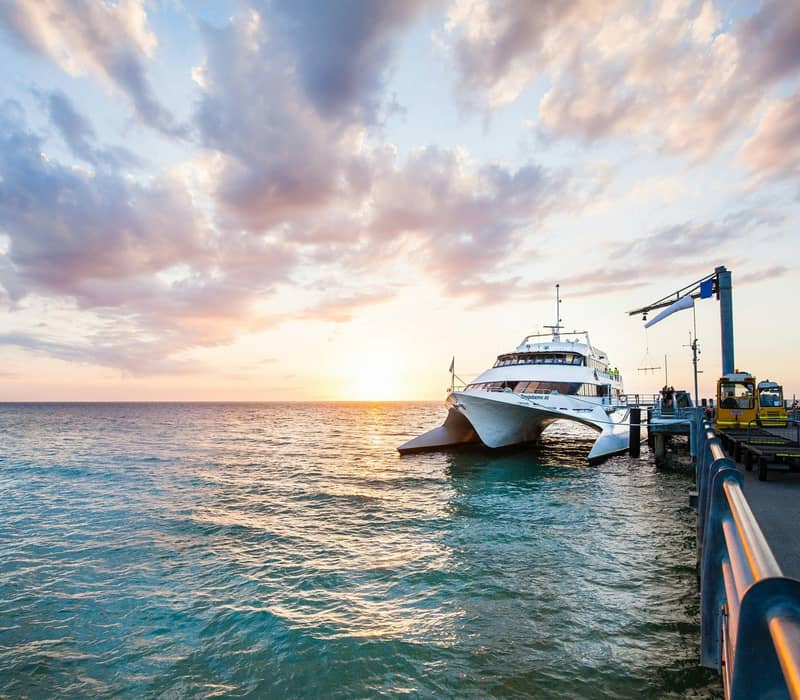 Ferry docked at jetty over ocean at sunset with partly cloudy sky.