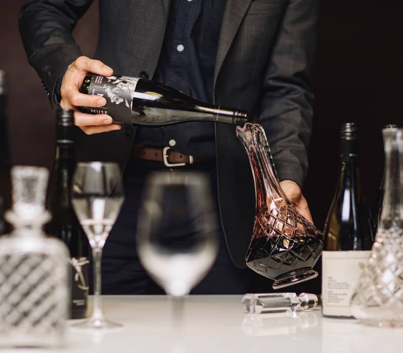 Close up of red wine being poured from a Moorilla bottle into a glass decanter.
