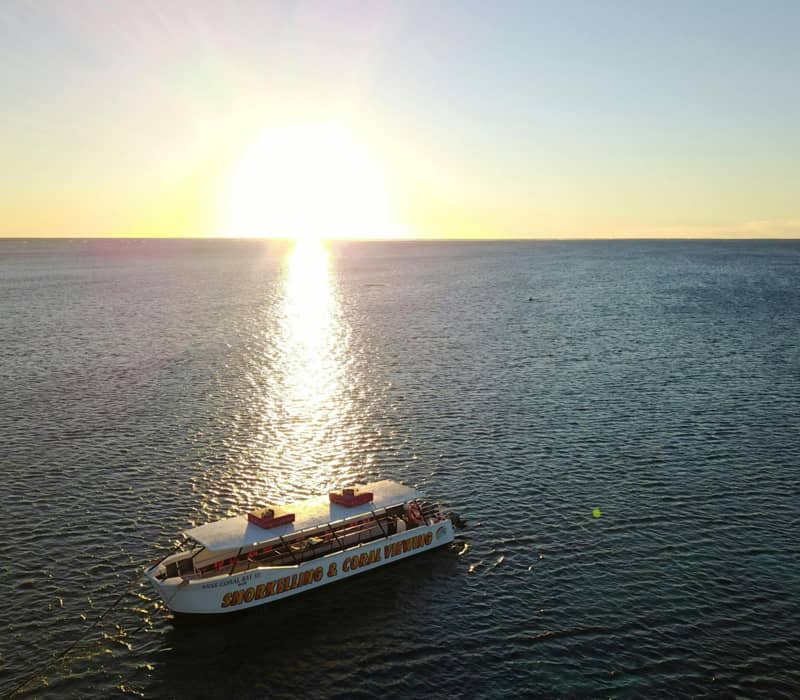 Aerial sunset view of a snorkelling and coral viewing boat on the calm sea in Coral Bay, WA.