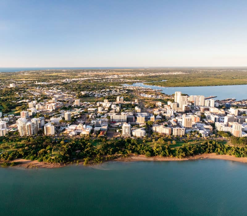 Aerial view of Darwin city waterfront, high-rise buildings, and lush green coastline in the Northern Territory.