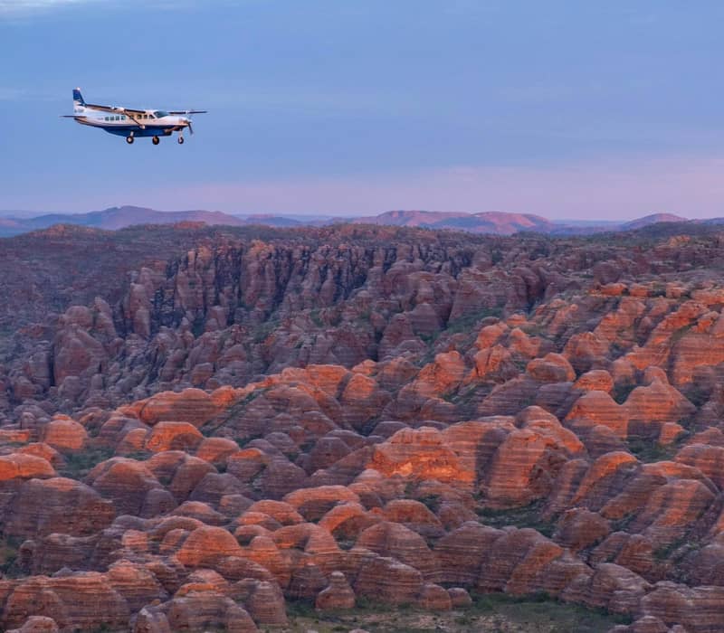Small Aviair plane flying over orange layered Bungle Bungles rock formations at sunset.