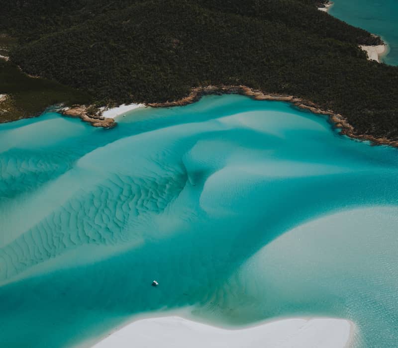 A breathtaking top-down aerial view of the iconic shifting white sands and vibrant turquoise water patterns at Hill Inlet on Whitehaven Beach.