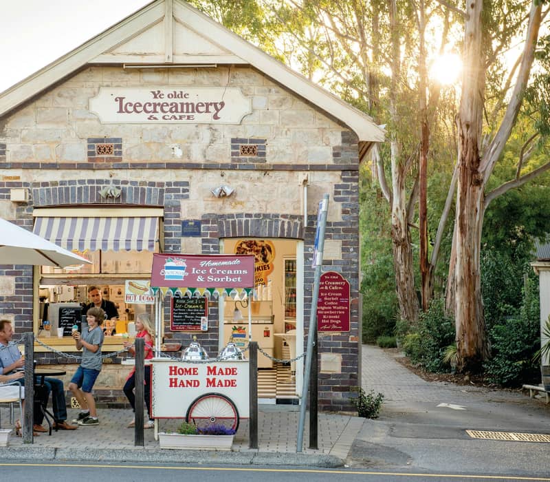 A family of four sitting at an outdoor table eating ice cream in front of a rustic stone heritage building in Hahndorf, South Australia.