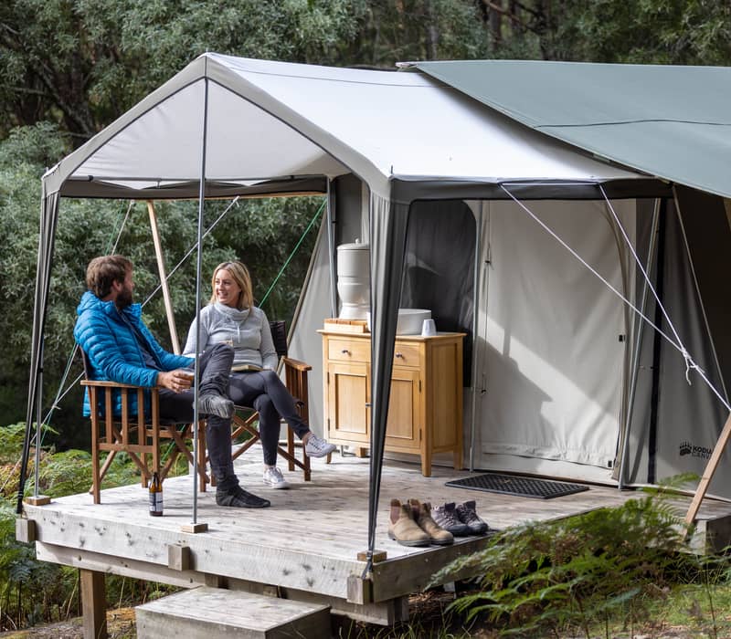 Group of people socializing on the deck of a wooden eco-cabin in the Tasmanian bush.