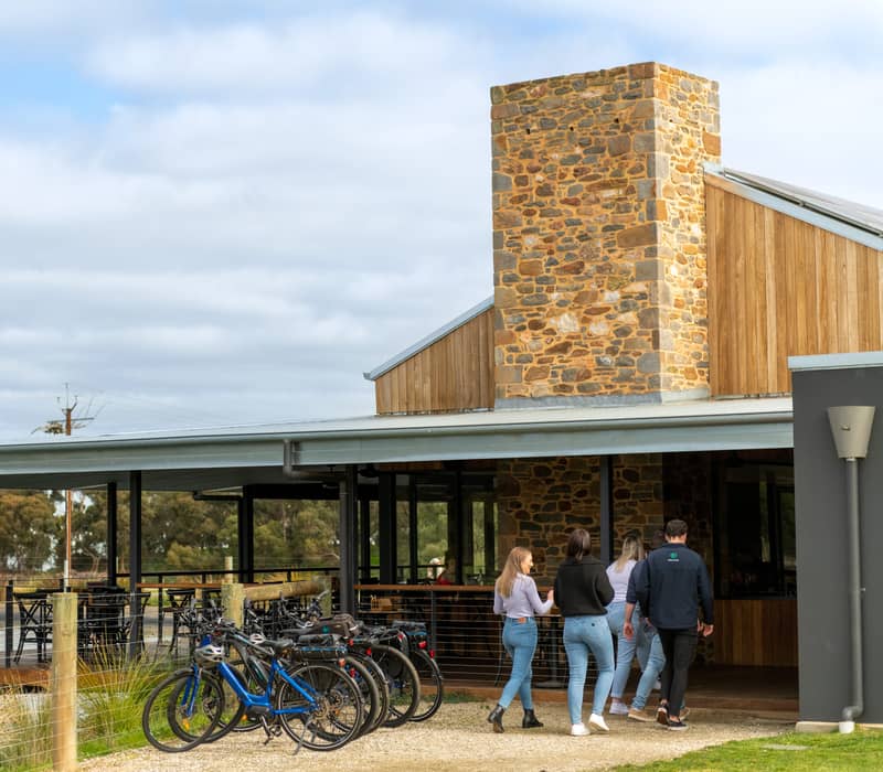 A group of cyclists walking toward a modern stone winery building with e-bikes parked in front.