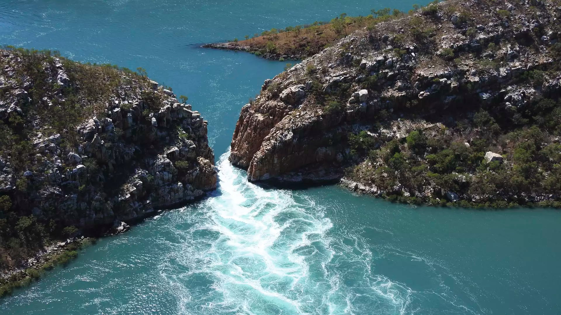 Aerial view of turquoise water rushing through a narrow gap between two rocky islands in the Kimberley, creating a waterfall effect.
