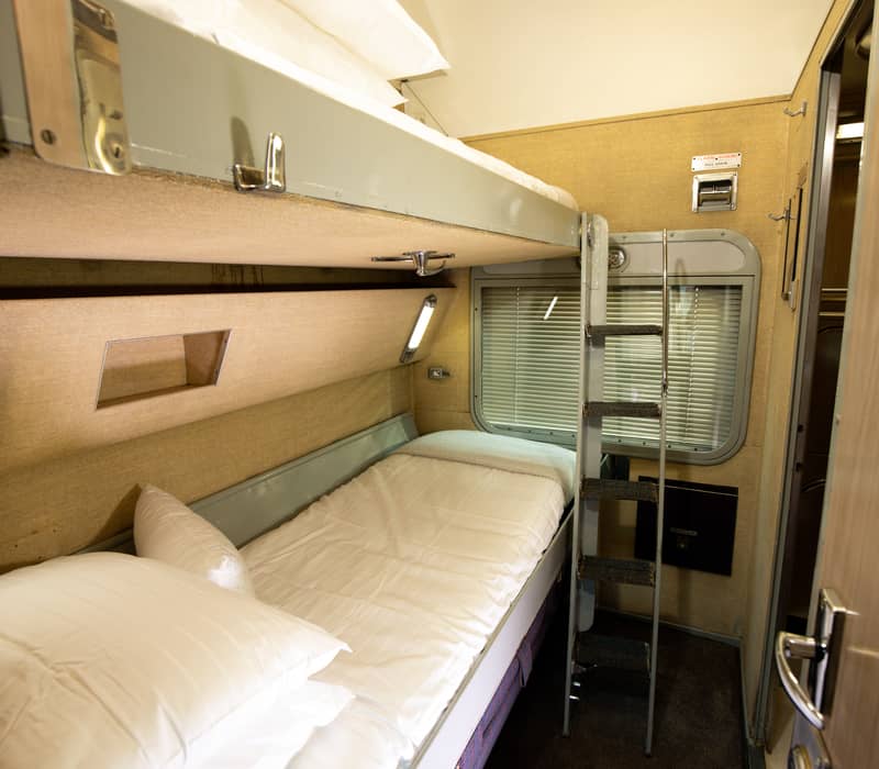 The interior of a vintage train sleeper cabin with two bunk beds and mid-century fixtures.
