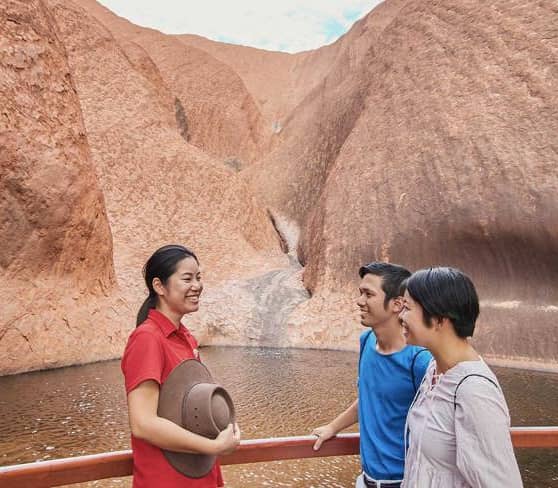Visitors at Mutitjulu Waterhole near Uluru with red rock formations.