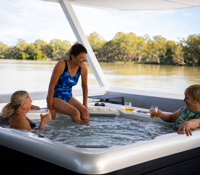 Three women enjoying a hot tub with drinks on the top deck of a luxury houseboat on the Murray River in South Australia.