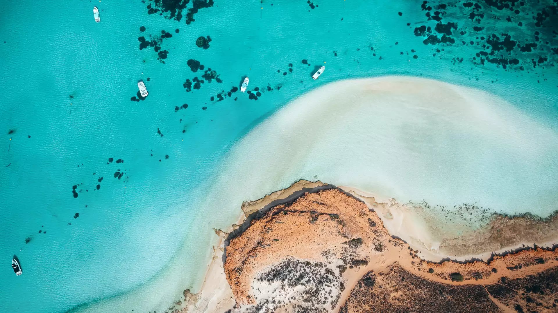 Aerial view of turquoise ocean channels winding through white sand banks and red earth in Shark Bay.