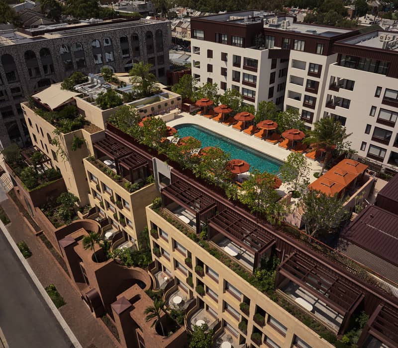 High-angle view of a modern hotel building featuring rooftop gardens, a swimming pool, and private terraces in Sydney.
