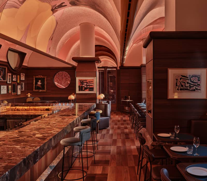 Atmospheric cocktail bar with a marble counter, vaulted illuminated ceilings, and dark wood panelling at Bar Julius.