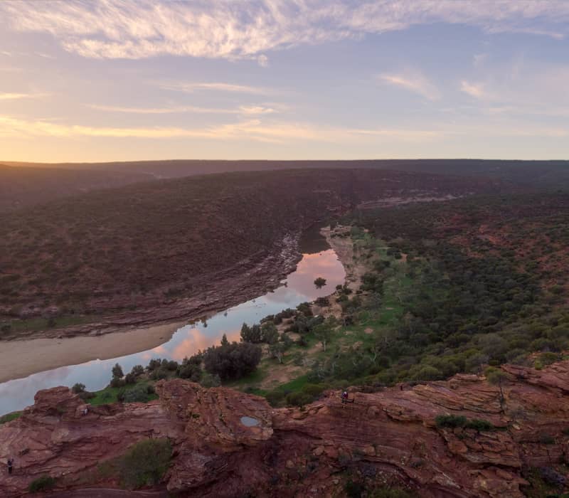 Aerial view of a winding river at the bottom of a deep red rock gorge during a soft pastel sunset.