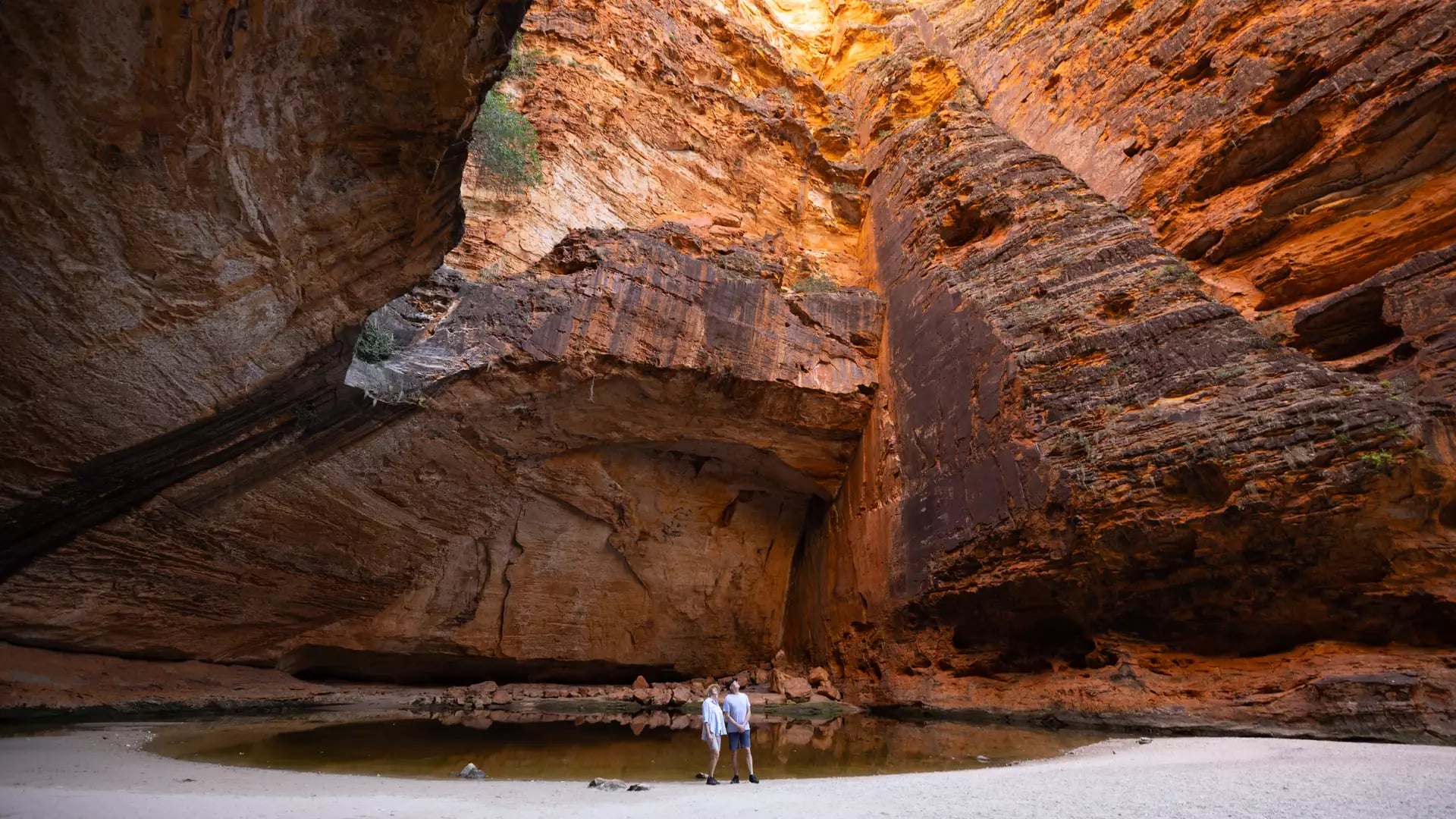 A wide interior shot of the orange rock walls of Cathedral Gorge reflecting in a dark pool of water.