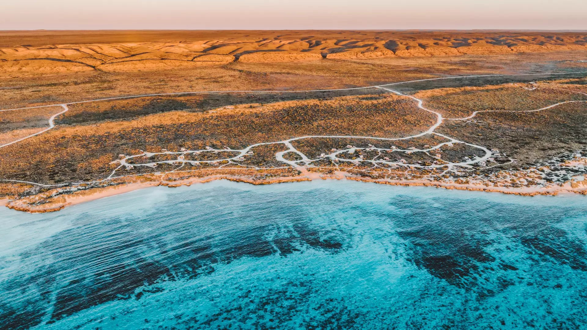 Aerial landscape of the Ningaloo Coral Coast showing the reef beneath clear blue water and the adjacent desert.