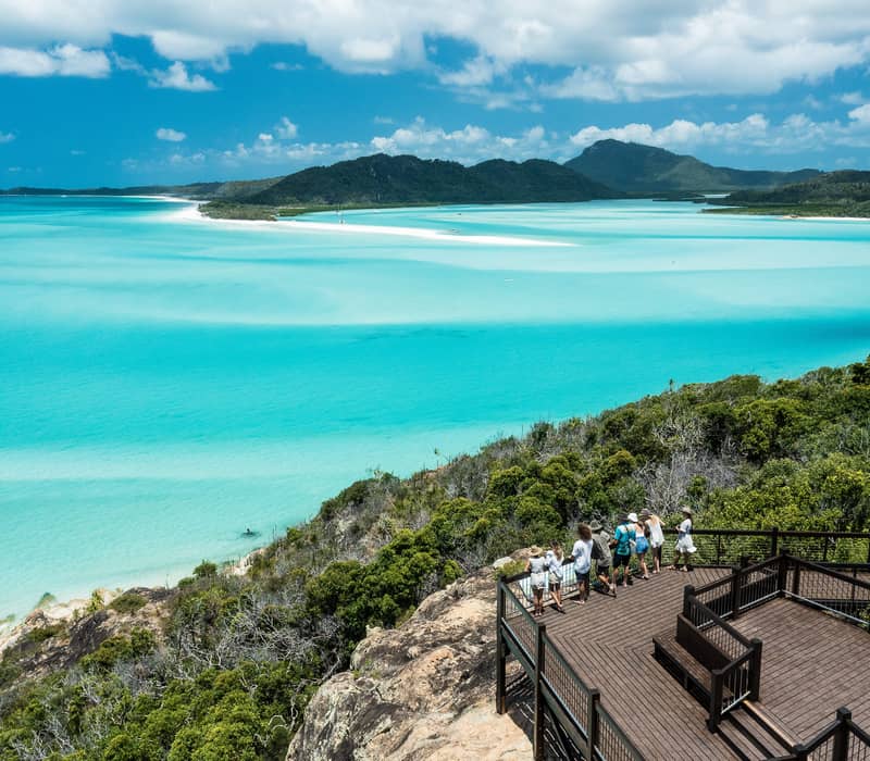 A group of people standing on a wooden lookout deck overlooking Hill Inlet and Whitehaven Beach.