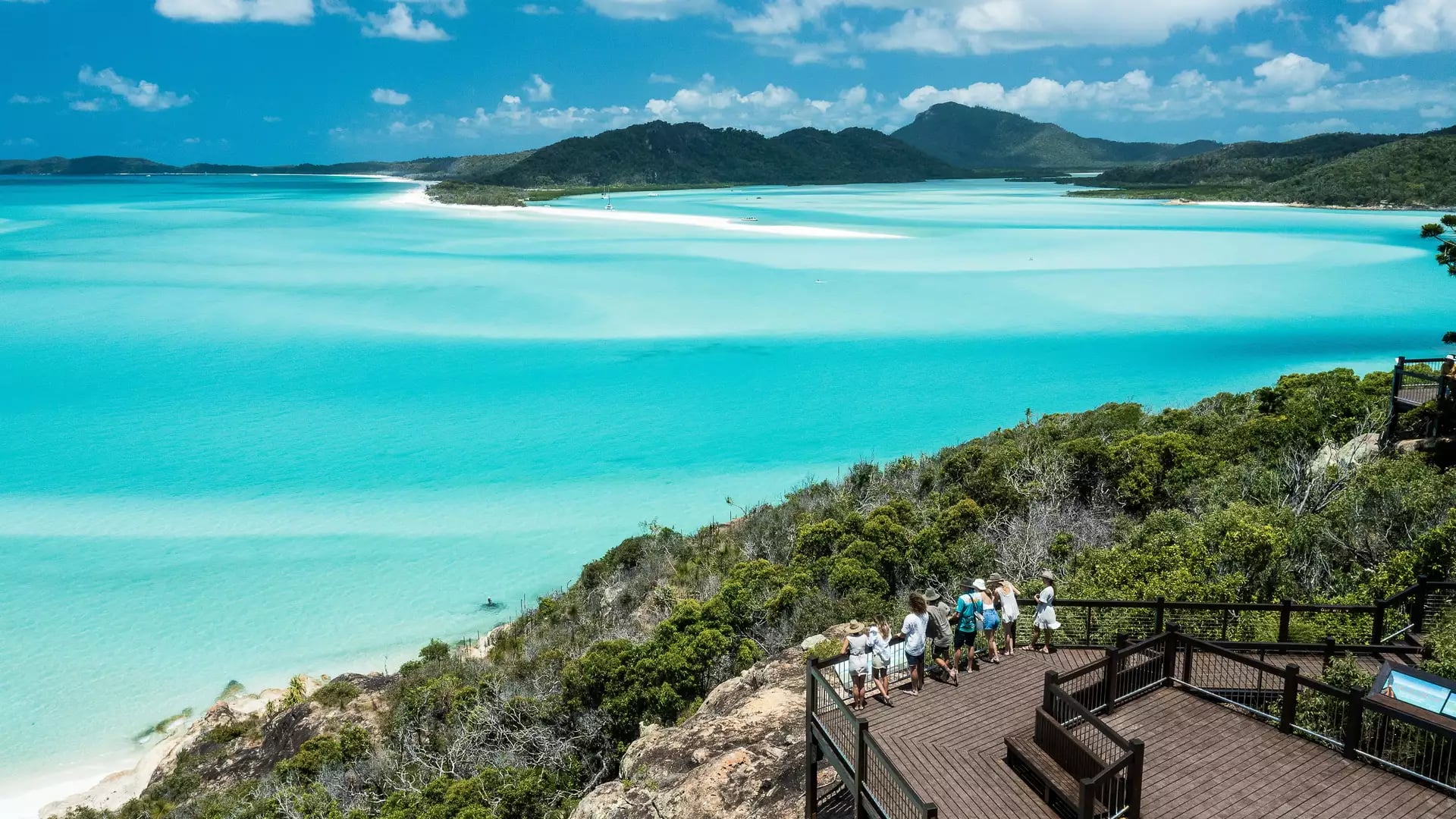 A group of people standing on a wooden lookout deck overlooking Hill Inlet and Whitehaven Beach.