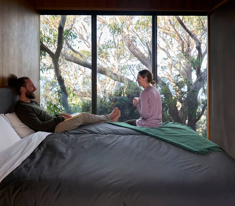 A modern eco-lodge with a long dining table and sofas nestled into the Tasmanian bush.