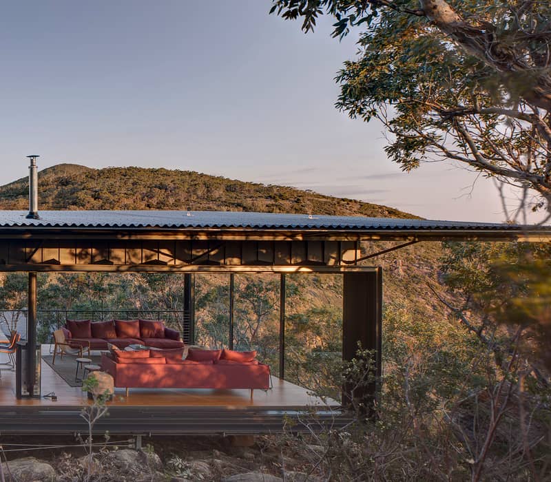 A modern eco-lodge with a long dining table and sofas nestled into the Tasmanian bush.