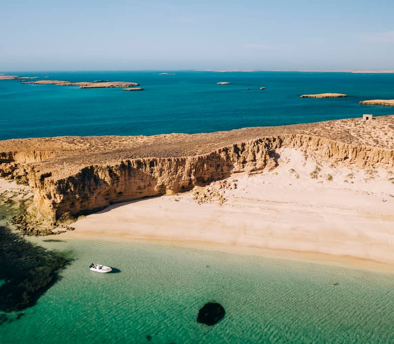Drone shot of a white beach and rocky cliffs at the Montebello Islands with a small boat in the water.