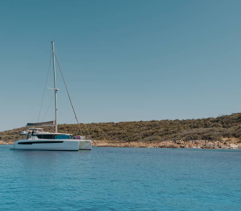 A large Eclipse Expeditions sailing catamaran anchored near a rocky shoreline under a clear blue sky in WA.