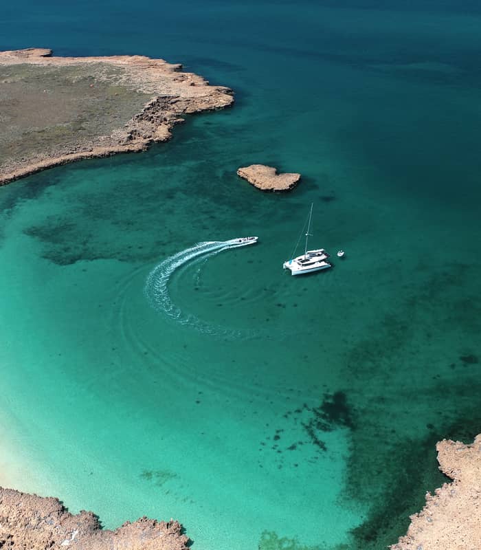 High angle drone shot of a white catamaran in a clear turquoise bay at Delta Island, Western Australia.