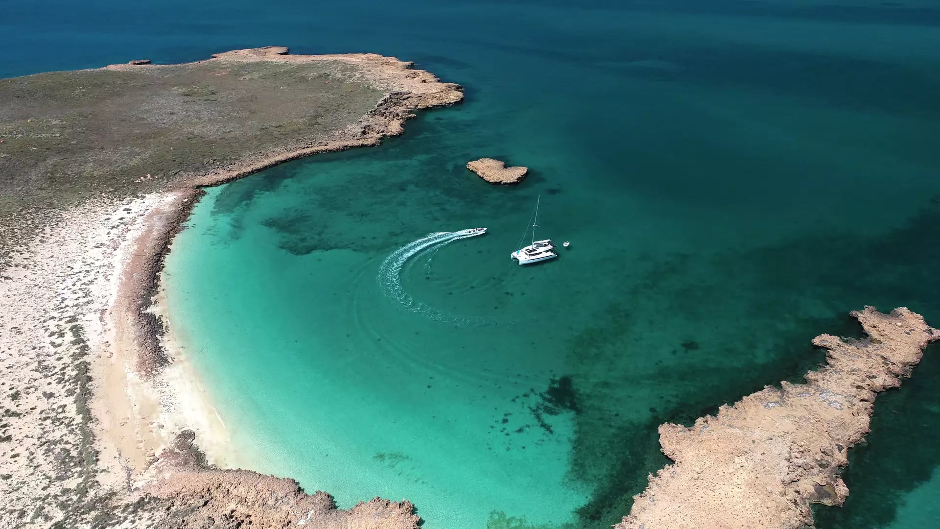 High angle drone shot of a white catamaran in a clear turquoise bay at Delta Island, Western Australia.
