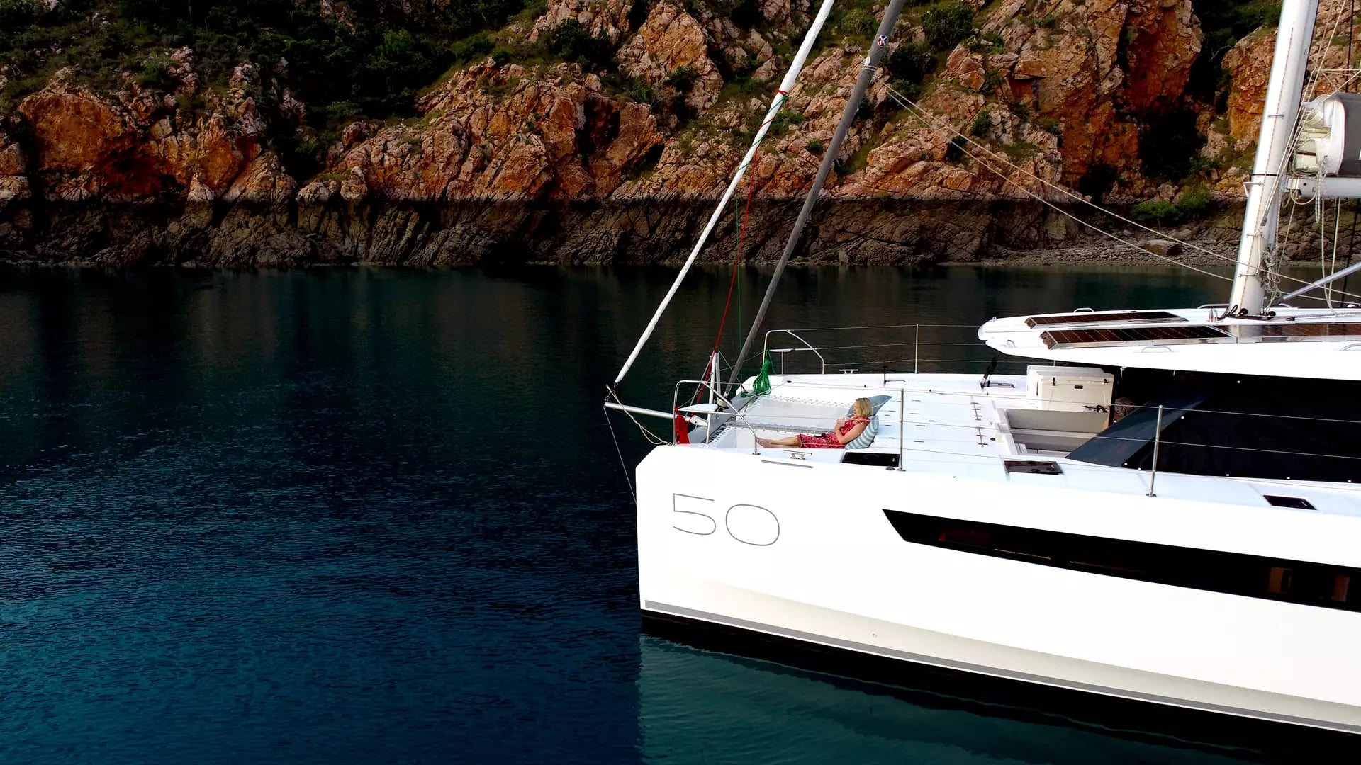 Woman relaxing on an Eclipse Expeditions luxury catamaran in front of red Kimberley cliffs at Dugong Bay.