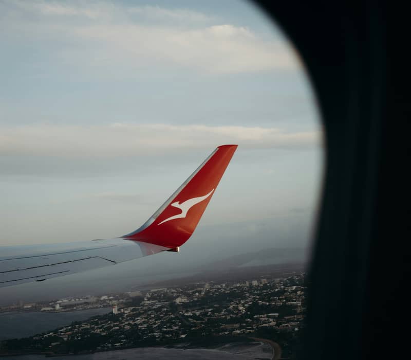View from a plane window of a Qantas winglet flying over the coastline and blue waters of Queensland.